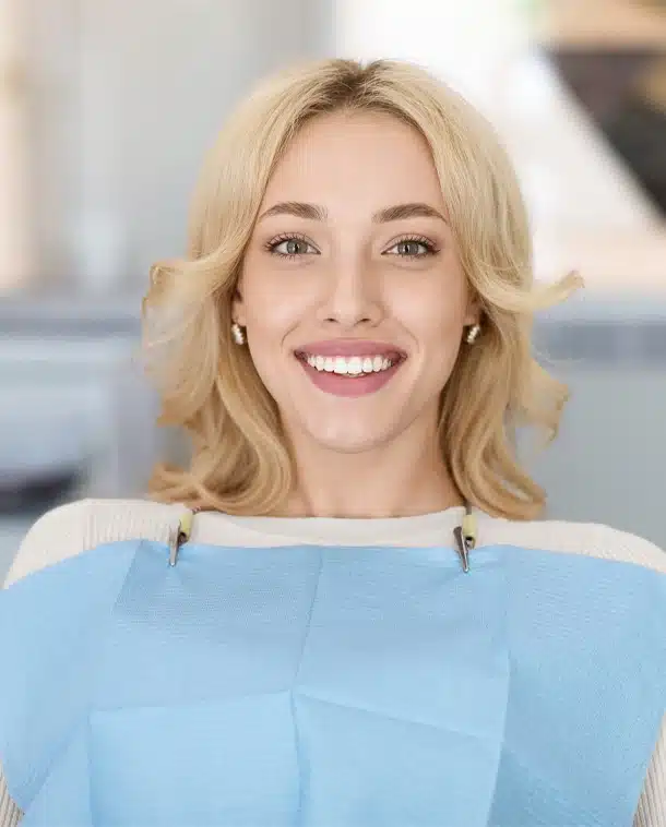 Smiling woman with blonde hair in light blue top, professional dental office setting.
